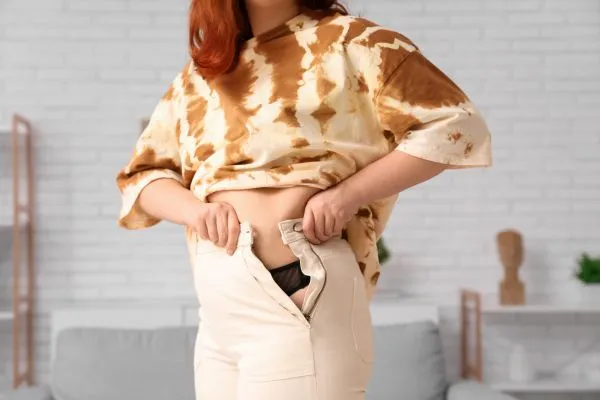 Image of woman trying to do her trousers up after pregnancy weight gain Headingley