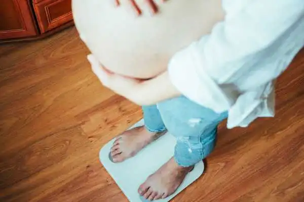 Image of woman weighing herself and experiencing weight gain through pregnancy Headingley