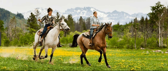 Confident plus-size woman riding Headingley a horse through a field with a smile on her face.